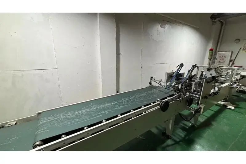 Long green conveyor beside machinery in a factory workspace.