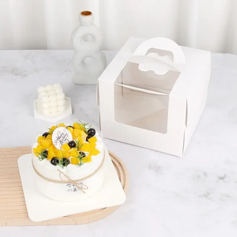 Decorated cake beside a white box with a clear window and handle.