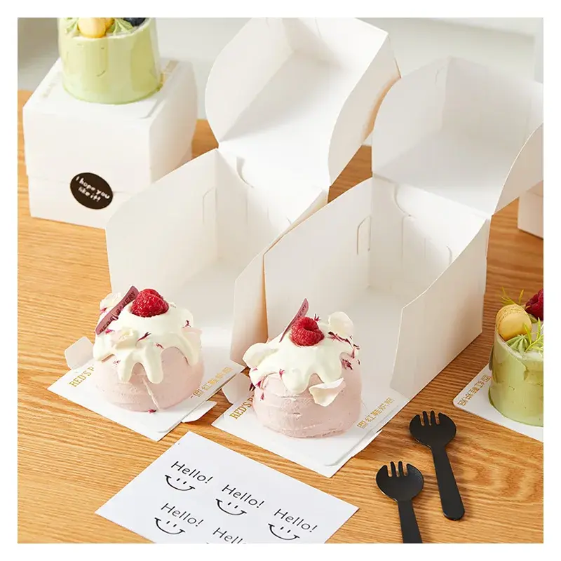 Small decorated cakes beside open white folding boxes.