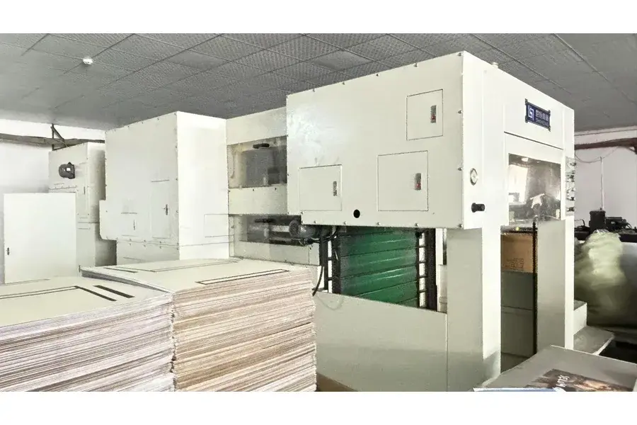 Large light-colored machine beside stacks of board sheets.
