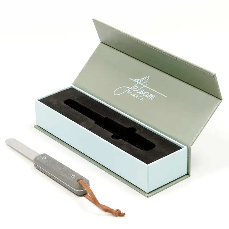 Open green presentation box beside a metal tool with a loop strap.