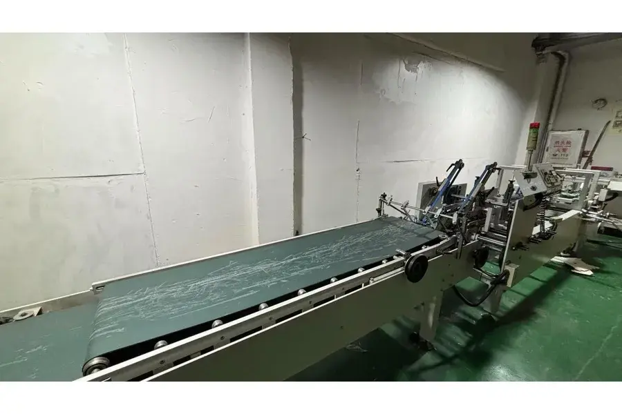 Green conveyor leading toward machinery in a factory room.