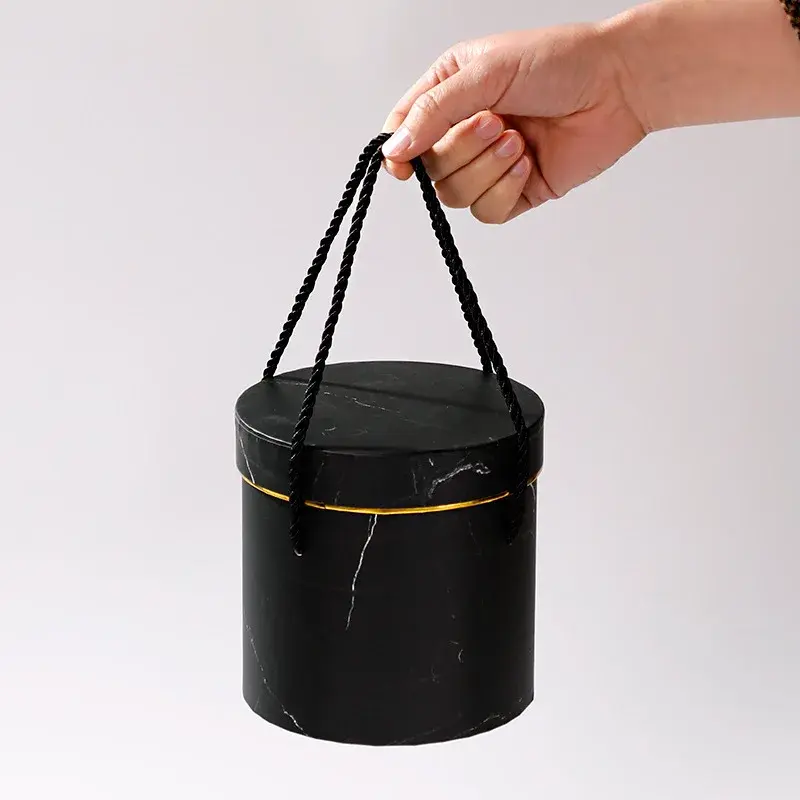 Hand holding a black cylindrical container by its cord handles.