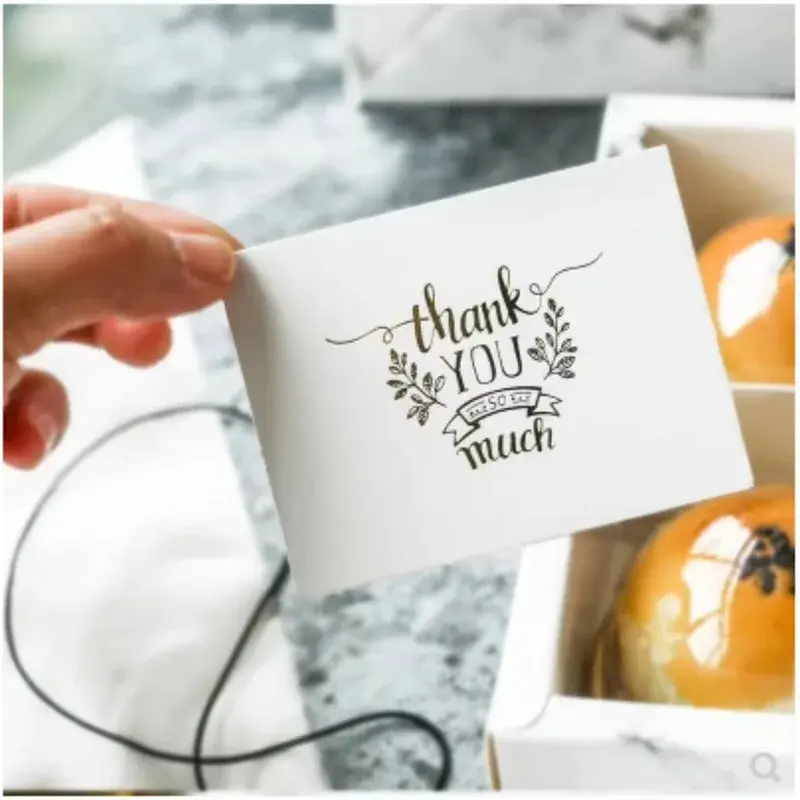 Hand holding a white card with decorative black thank-you lettering.