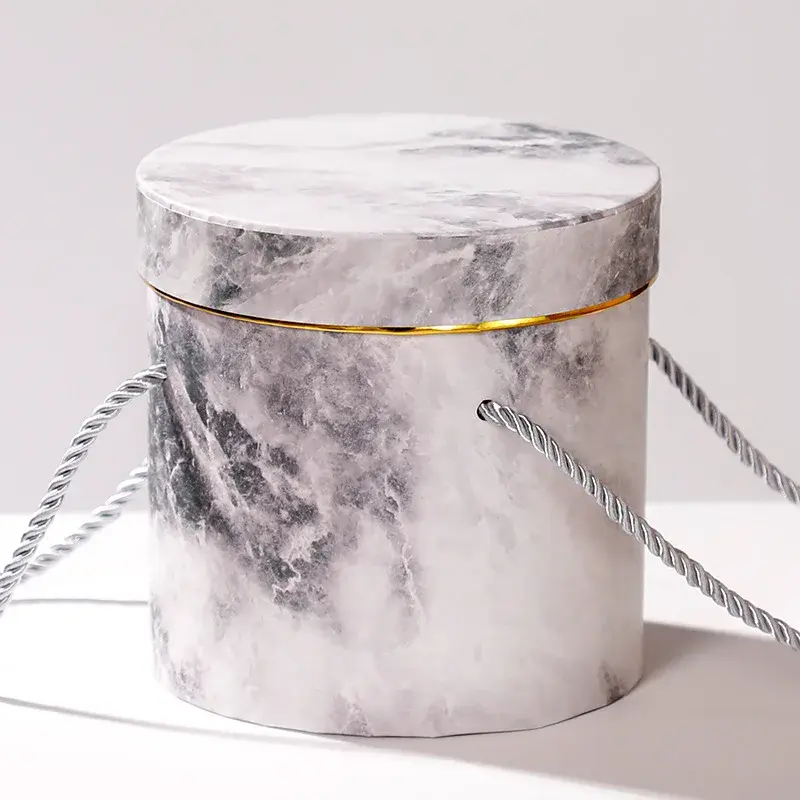 Marble-patterned cylindrical box with cord handles and a gold line.