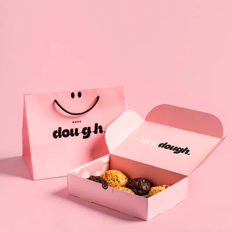 Pink cookie box with its lid open beside a matching shopping bag.