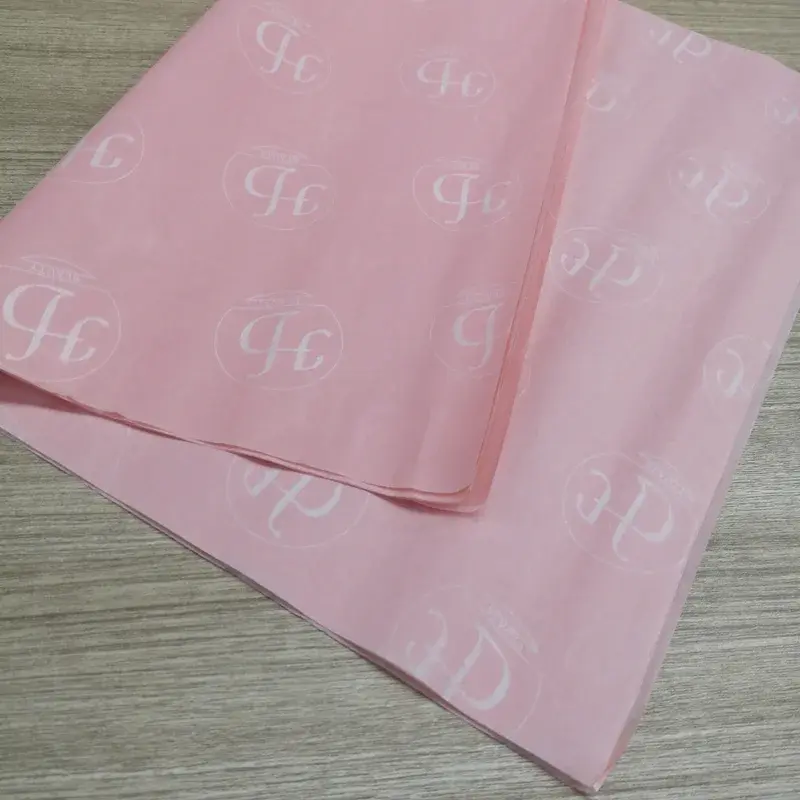 Pink tissue sheets with repeating pale monogram lettering.