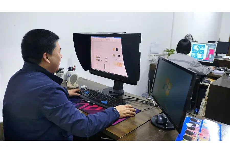Worker using a computer and control panel beside printing equipment.