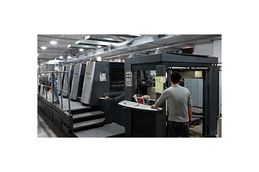 Long printing machine with a worker in a factory workspace.
