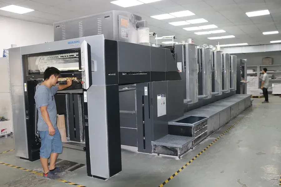 Worker beside a large printing press in a bright factory room.
