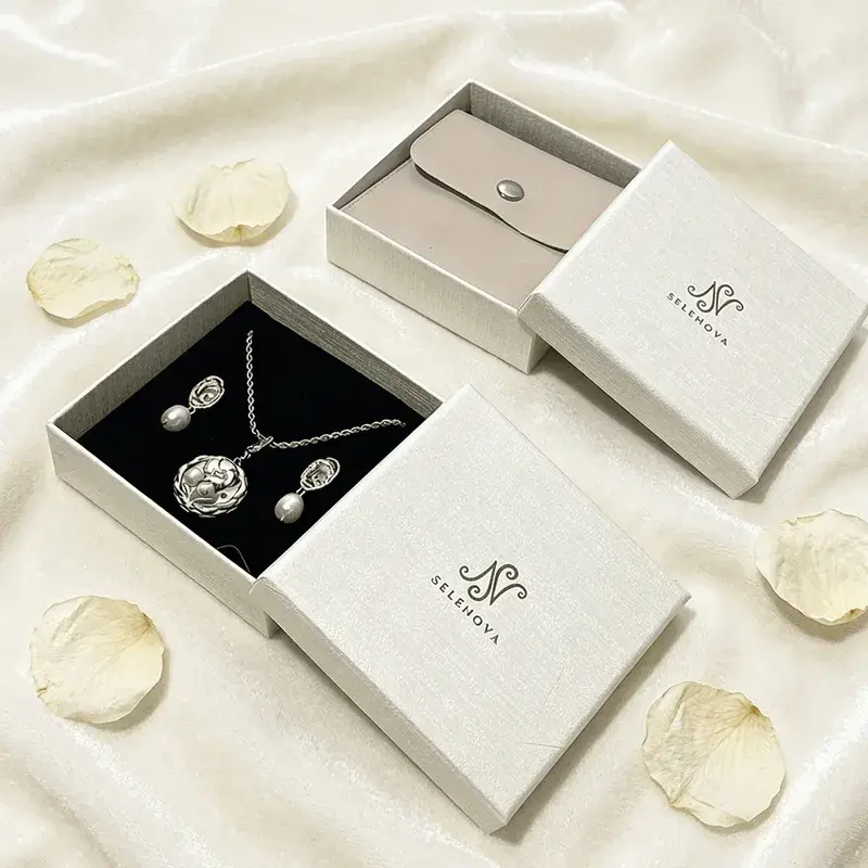 White jewelry boxes with black inserts holding necklaces and earrings.