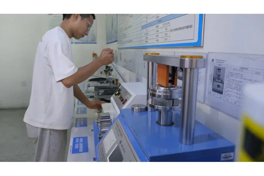 Worker operating a blue testing machine at a workbench.